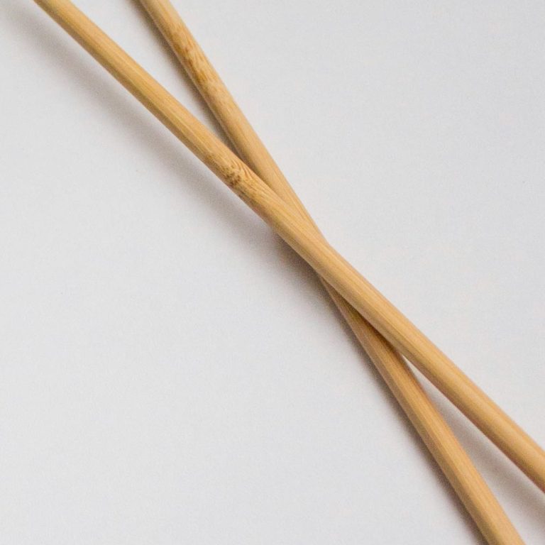Zwei Sticknadeln liegen sich kreuzend auf einer weißen Oberfläche.